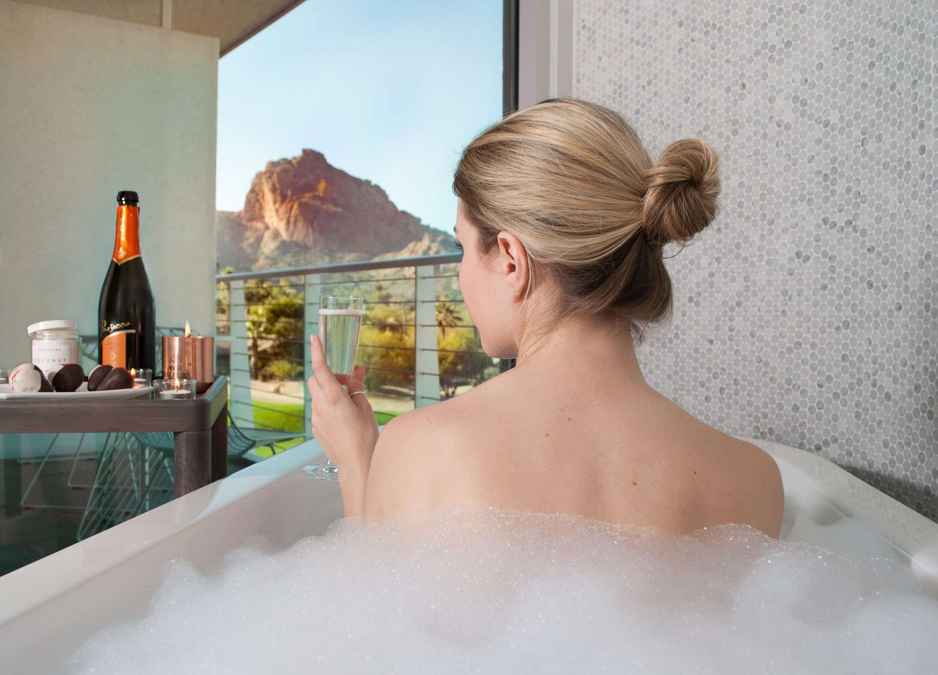 Woman in a bathtub covered in bubbles holding a champagne glass.