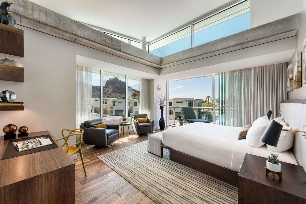 a bedroom with chairs, tables, and a large sliding glass door to the balcony