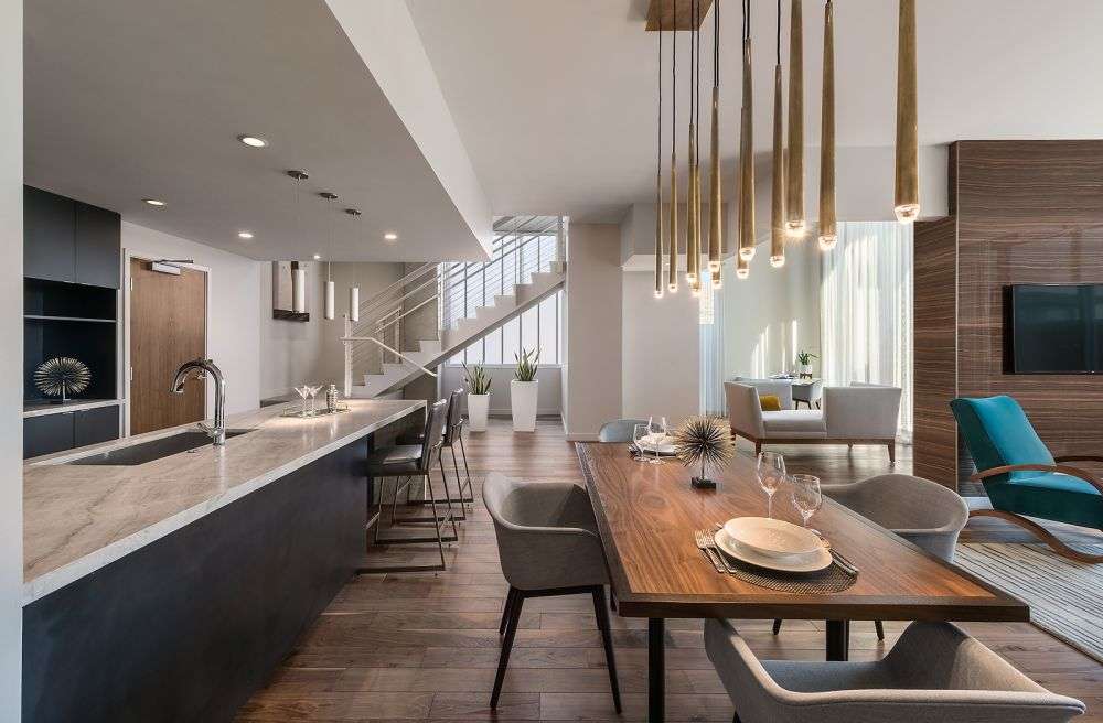 a room featuring a long dining table, hanging lights, and sitting area