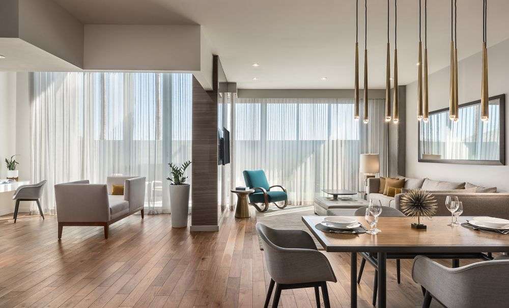 a room featuring a dining table, hanging lights, and large glass windows covered by curtains