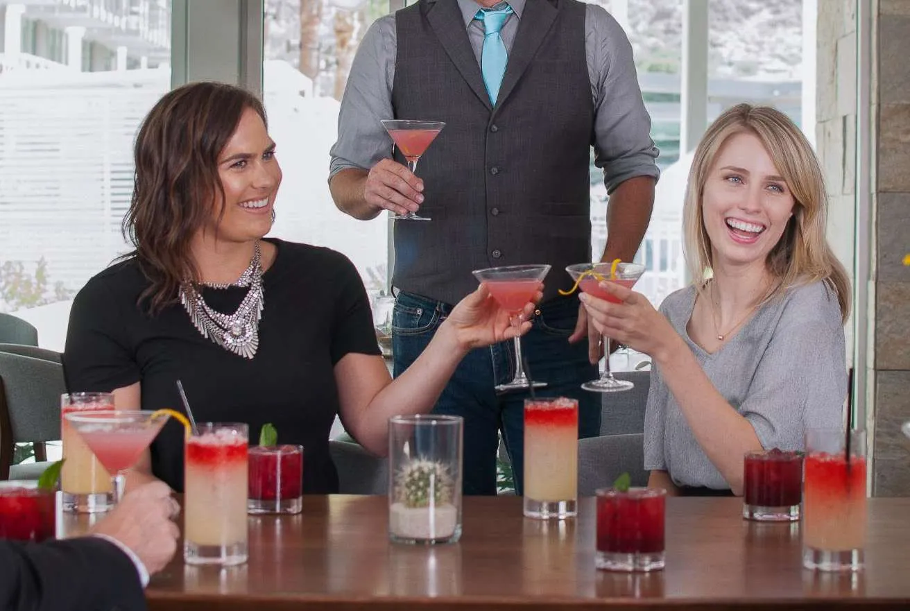 Two women smiling and sitting at a table holding drinks.