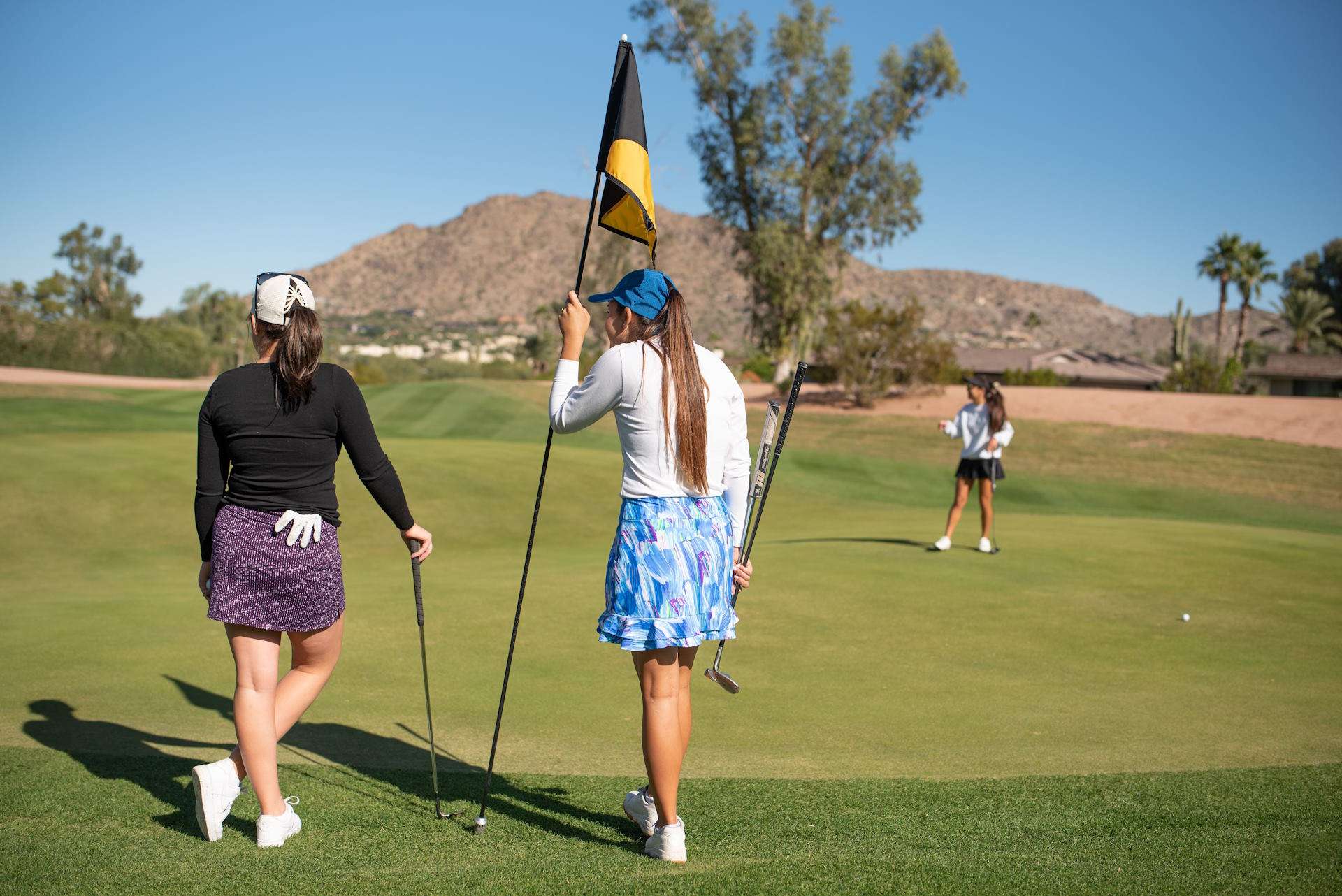 A group of women standing outside on a golf course.