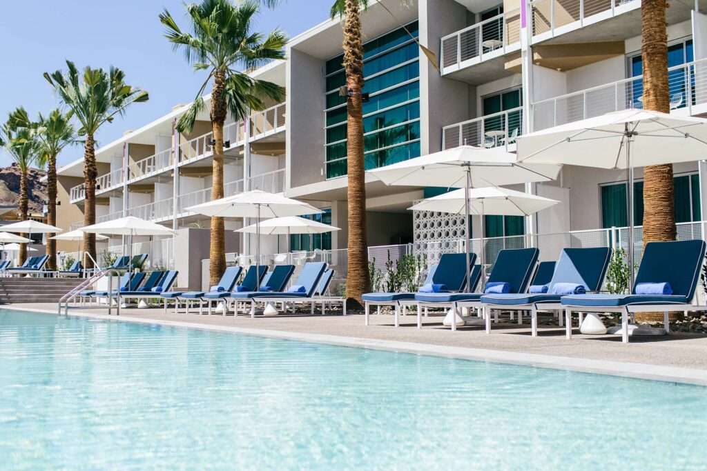 Chairs with umbrellas next to a large rectangular pool with buildings in the back.