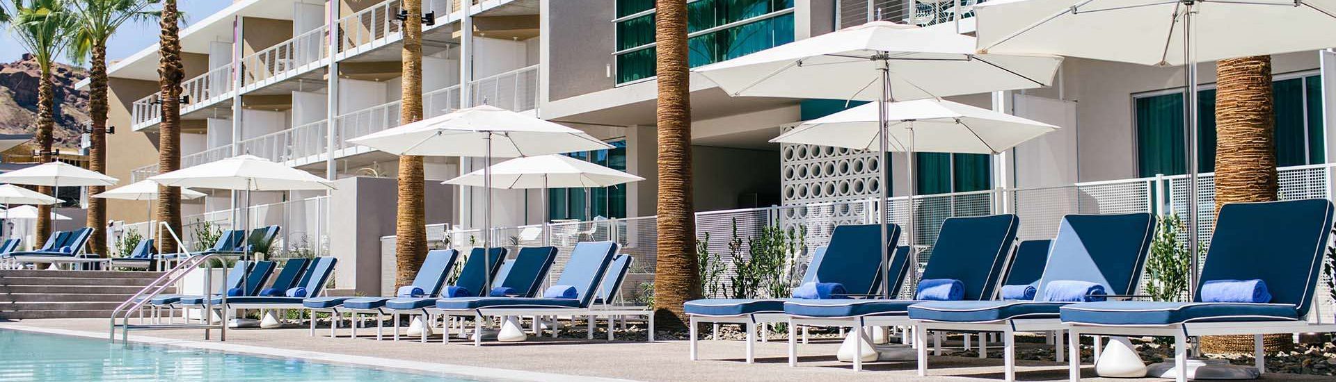 Chairs with umbrellas next to a large rectangular pool with buildings in the back.